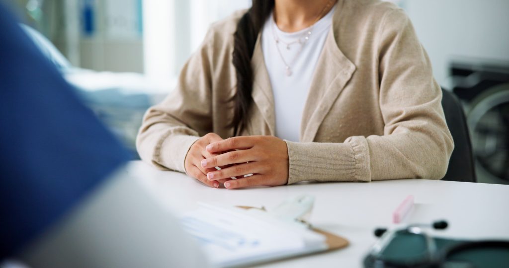 A close-up of a patient's hands resting on a table during a consultation in a medical setting.